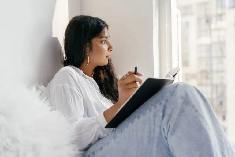 Ascendente Virgo: personalidad, aspecto y relaciones Mujer con ascendente Virgo escribiendo con calma en su libreta junto a la ventana