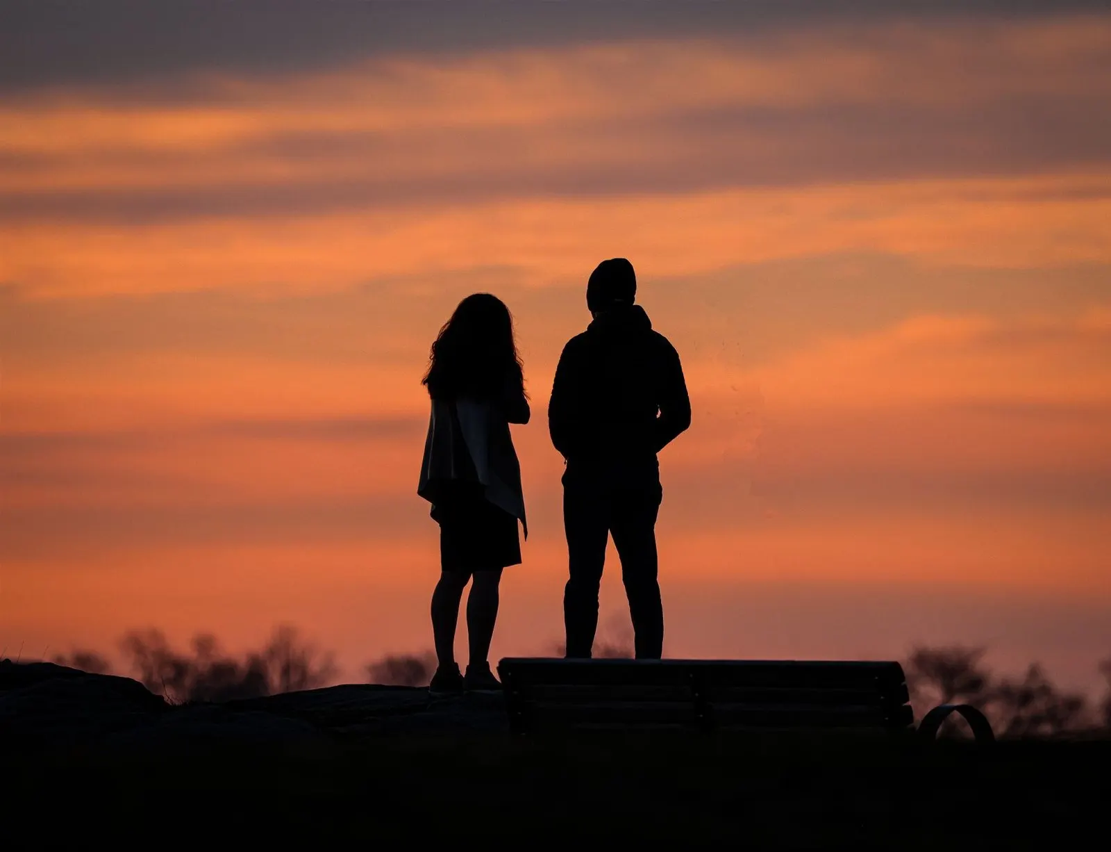 Dos personas conversando en un banco al atardecer, la pareja ideal de Géminis