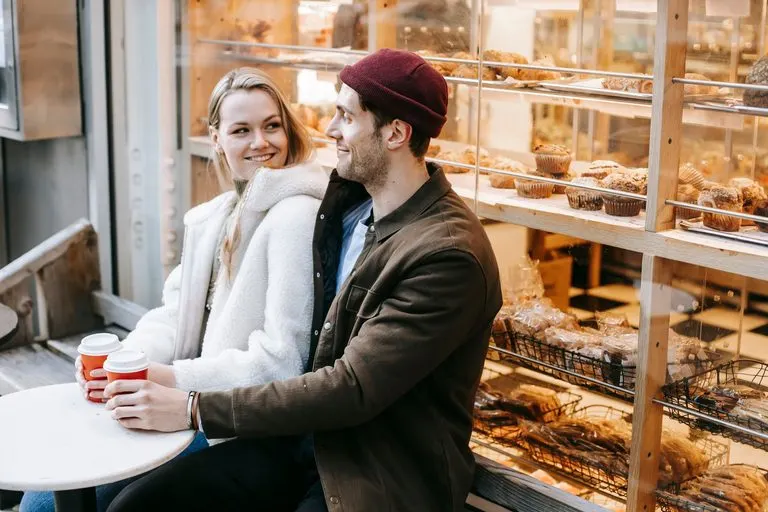 Pareja riendo durante una conversación en una cafetería, reflejo de Géminis alma gemela