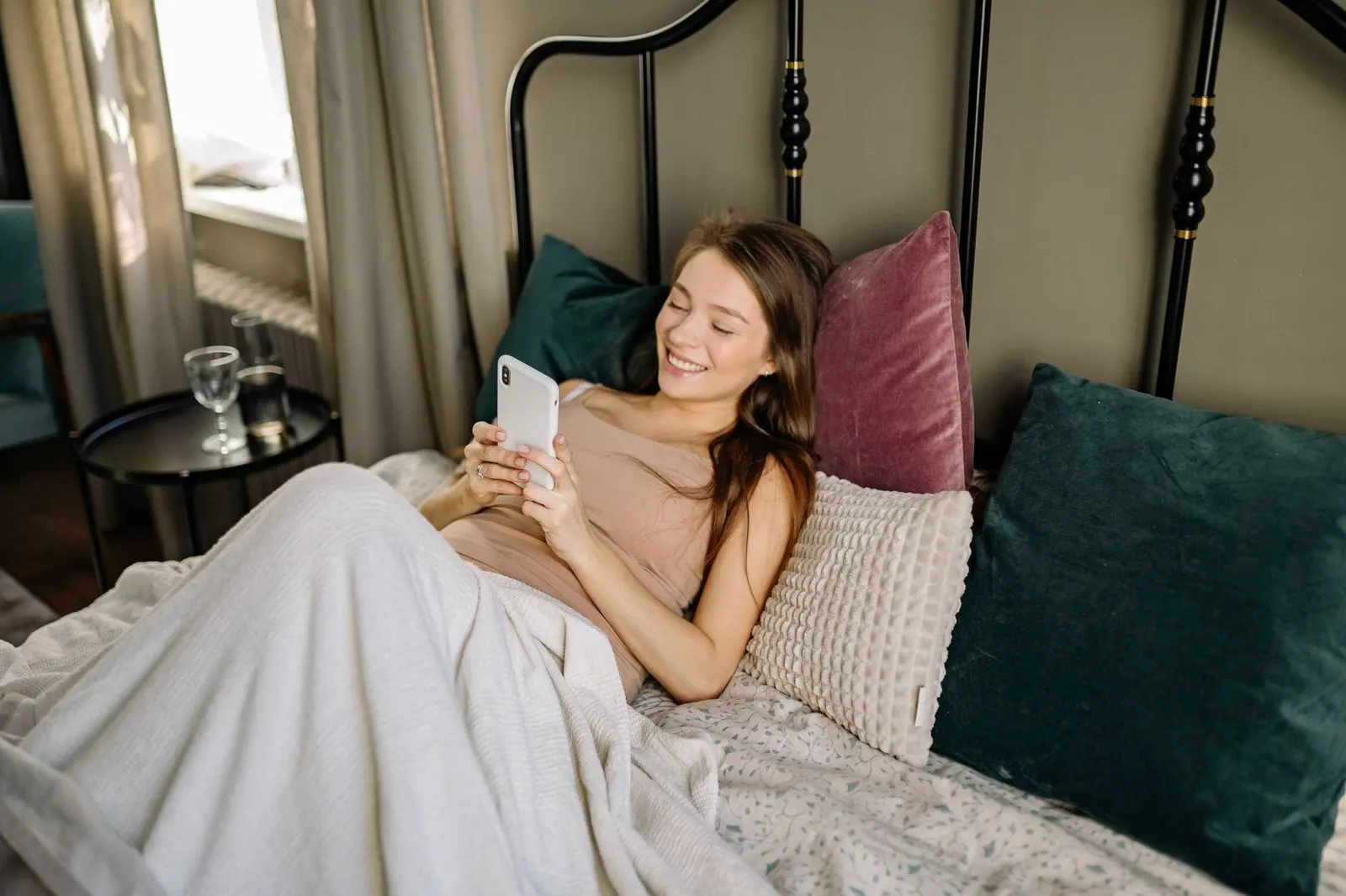 Mujer sonriendo mientras escribe un mensaje en la cama, complicidad geminiana