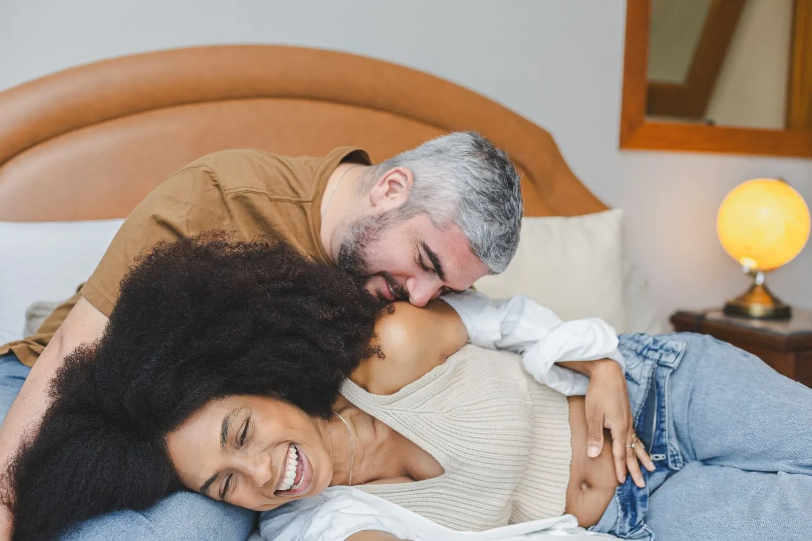 Pareja riendo abrazada entre sábanas blancas, así es Géminis en la cama