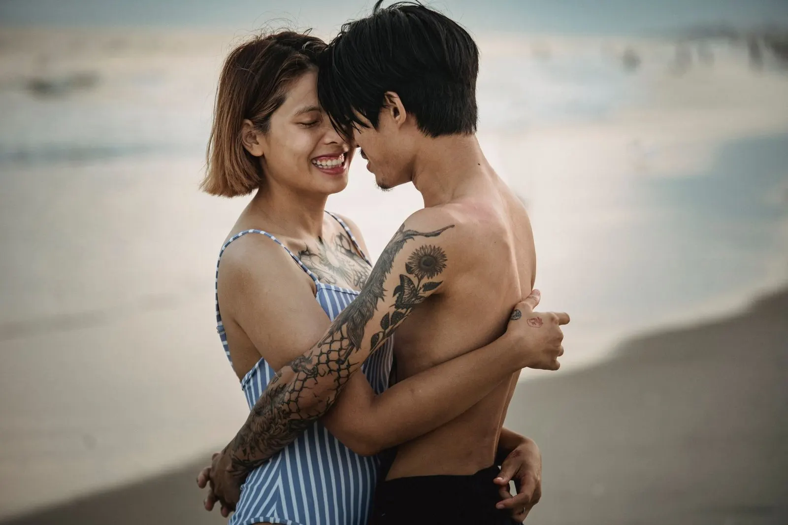 Hombre Aries y mujer Piscis abrazados frente al mar al atardecer