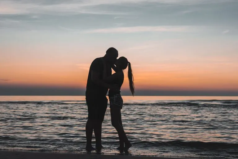 Hombre Leo y mujer Piscis abrazados frente al mar al atardecer