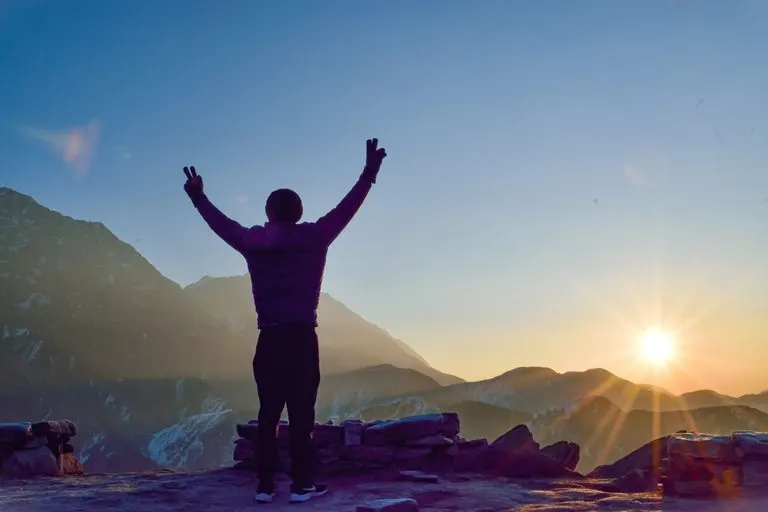 Mujer en la cima de una montaña al amanecer, símbolo del nodo norte en Aries