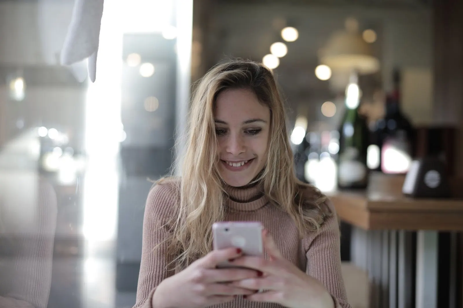 Hombre sonriendo mientras escribe un mensaje en una cafetería, señal de Géminis que extraña