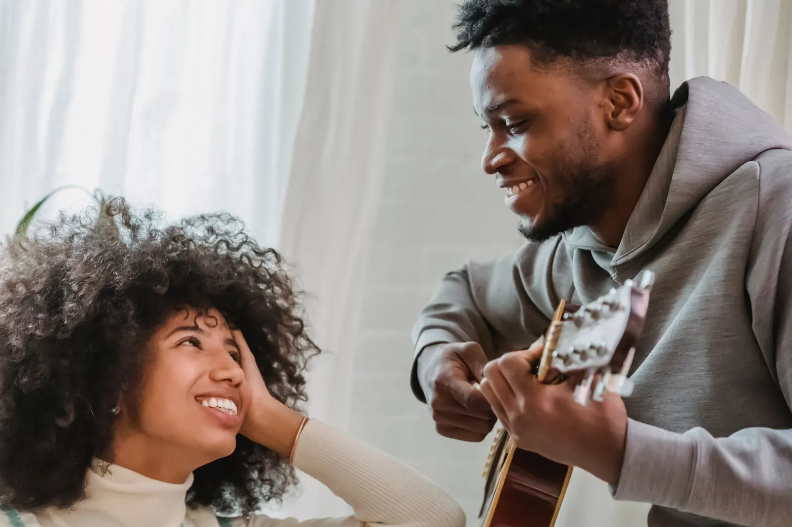 Mujer escuchando con cariño a su pareja tocar la guitarra en casa