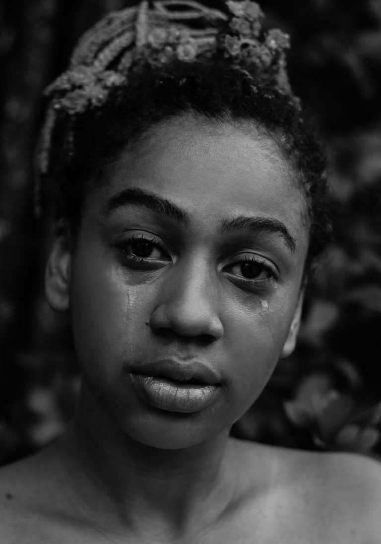 A black and white portrait of a young woman expressing deep emotion with tears.