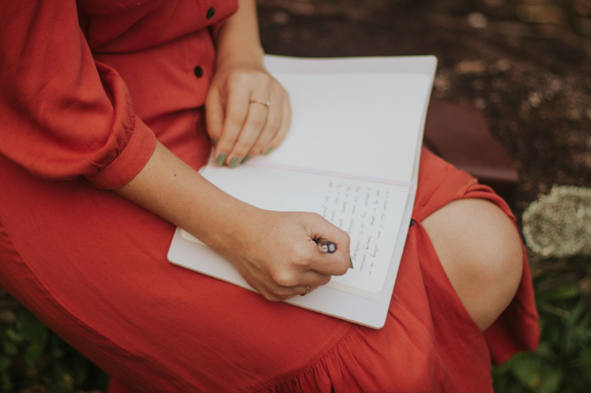 Mujer con vestido rojo escribiendo en un cuaderno al aire libre