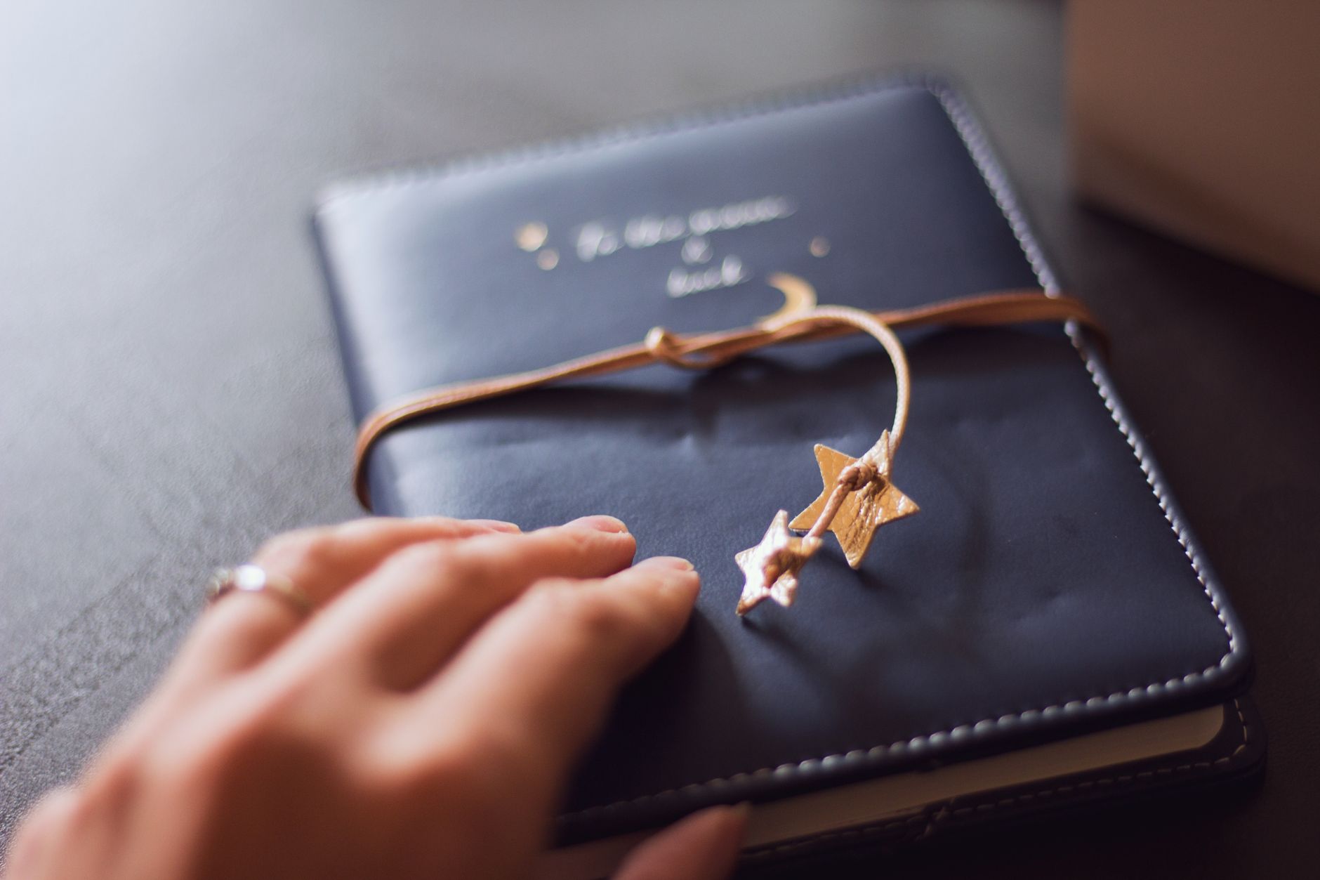 Ritual de luna nueva para aclarar tu intención Mano junto a un cuaderno negro con marcapáginas de estrellas doradas